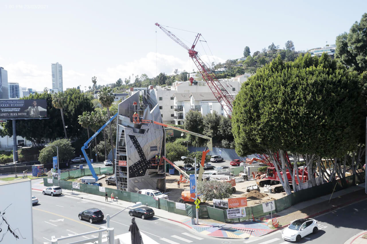 image of construction site of the new structure. Image includes a crane, cars, and trees at sunset spectacular
